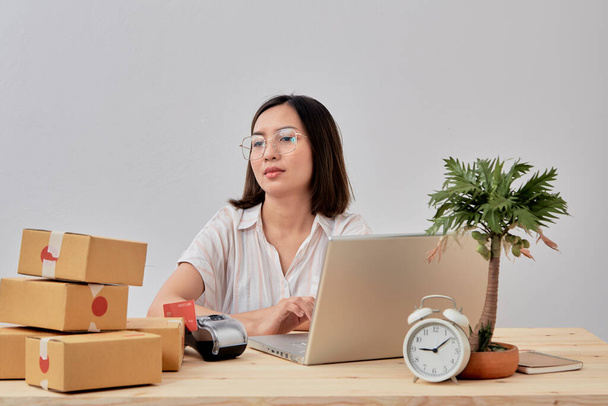 Молода приваблива азіатська жінка онлайн-продавець працює на замовлення перевірки ноутбуків в Інтернеті вдома, готуючись до доставки з дому
 - Фото, зображення