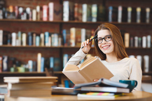 Молодая улыбчивая женщина учится дома со многими книгами
 - Фото, изображение