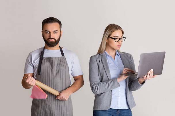 Wife in formal suit with glasses and with laptop in hands, man in apron and with rolling pin - Foto, Imagem
