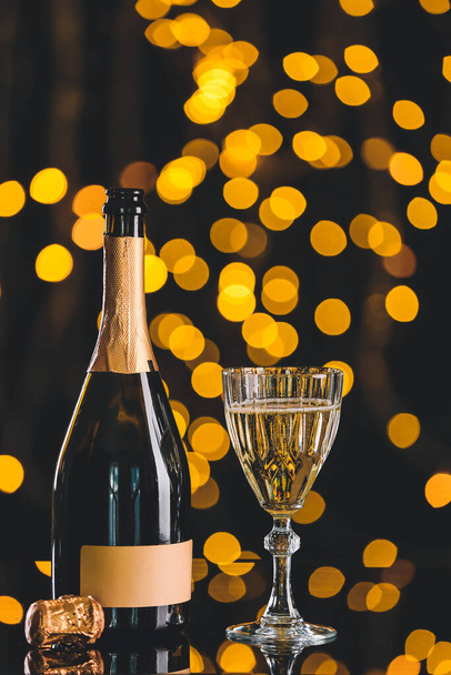 Glass and bottle of tasty champagne on dark background with blurred lights - Photo, Image