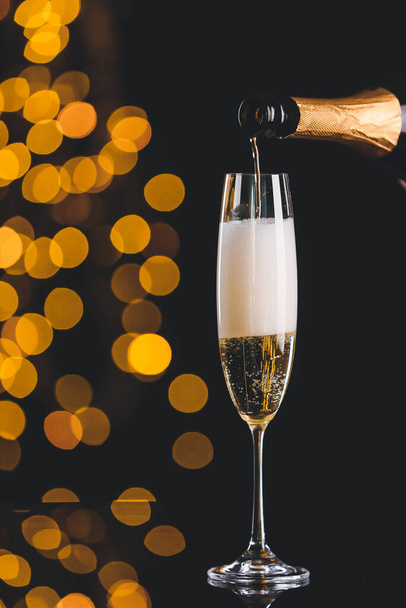 Pouring of champagne in glass on dark background with defocused lights - Fotoğraf, Görsel