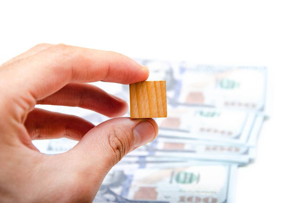 Wooden cubes and dollar bills. Male hand holds one wooden cube in the background dollar bills - Foto, immagini