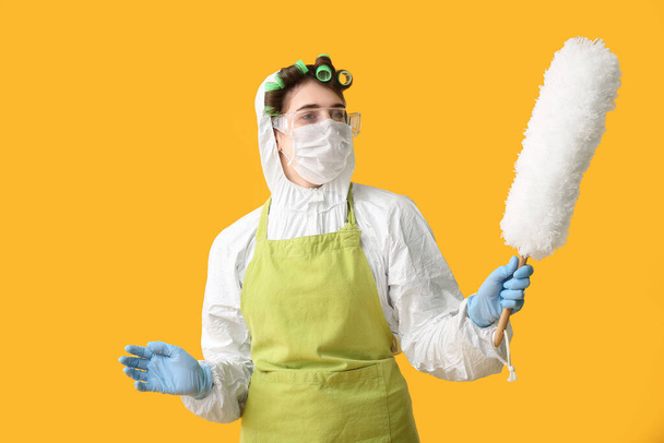 Νοικοκυρά σε προστατευτική ενδυμασία και με βούρτσα σκόνης στο φόντο χρώμα - Φωτογραφία, εικόνα