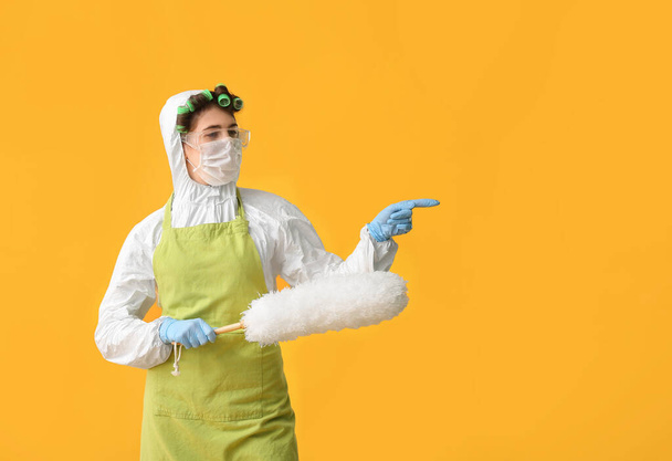 Νοικοκυρά με προστατευτική ενδυμασία και με βούρτσα σκόνης που δείχνει κάτι στο φόντο χρώμα - Φωτογραφία, εικόνα
