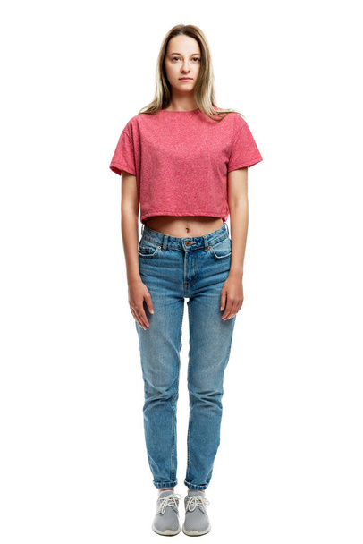 Serious young girl in a red tank top and jeans. Full height. Isolated on a white background. Vertical. - 写真・画像