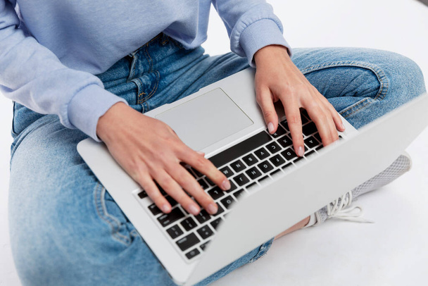 A young girl in jeans sits with a laptop on her lap. Blogging and communication. White background. - Фото, изображение
