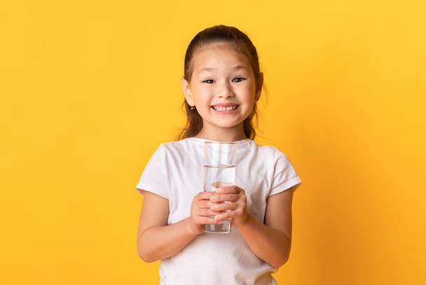 Портрет веселого азиатского ребенка, держащего стакан пресной воды
 - Фото, изображение