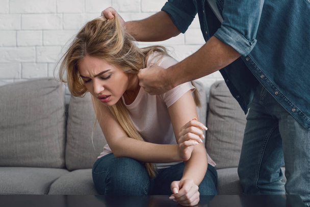 Ο άντρας απειλεί τη γυναίκα αρπάζοντας τα μαλλιά της, το γυναικείο πρόσωπο εκφράζει πόνο - Φωτογραφία, εικόνα