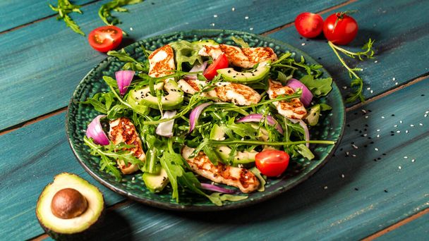 Verse saladeplaat met arugula, halloumi kaas, tomaten en avocado houten ondergrond van dichtbij. Gezond eten. Groene meel. - Foto, afbeelding