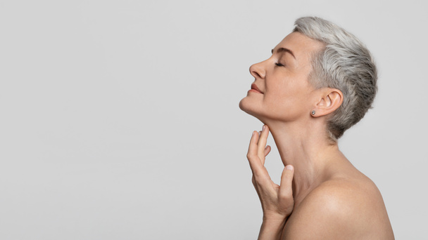Anti-Age-Behandlung. Schöne Frau mittleren Alters berührt weiche Haut am Hals - Foto, Bild