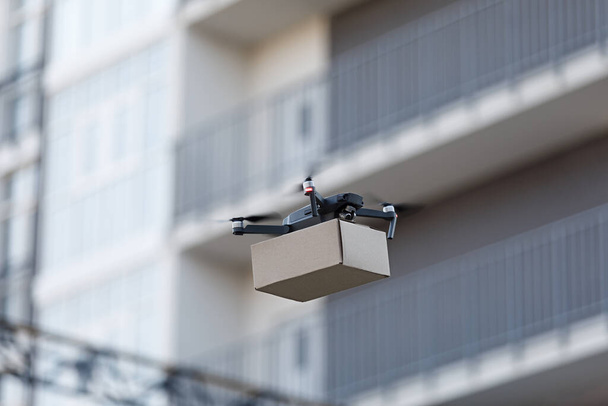 Flying Drone sosteniendo el paquete. Entrega de aire a través de la ciudad
 - Foto, Imagen