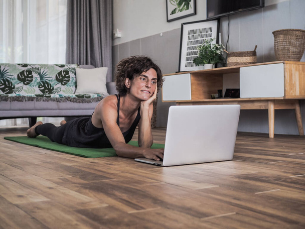happy woman using laptop at home lying on yoga mat - Фото, зображення