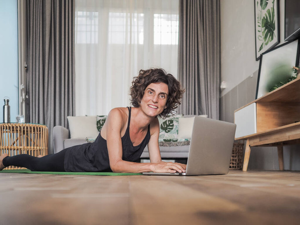happy woman using laptop at home lying on yoga mat - Fotó, kép
