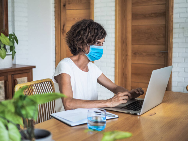 woman wearing mask working with laptop at home, home office and quarantine concept - Foto, imagen