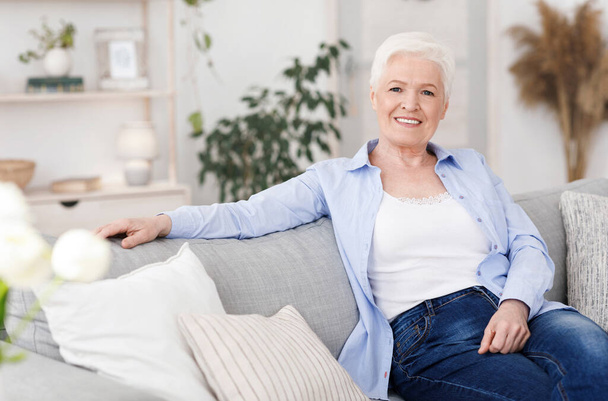 Hymyilevä vanha nainen poseeraa sohvalla olohuoneessa kotona - Valokuva, kuva