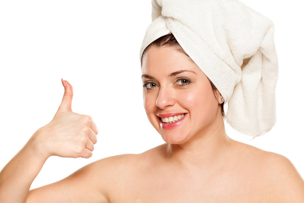 Jovem mulher bonita com toalha na cabeça no fundo branco mostrando polegares para cima
 - Foto, Imagem