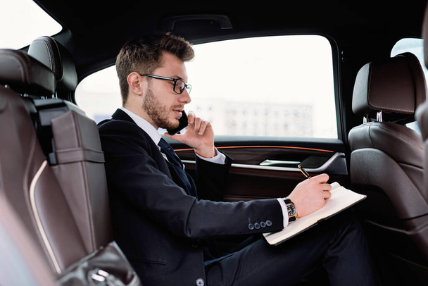 Empresario escribiendo en cuaderno en coche de lujo
 - Foto, Imagen