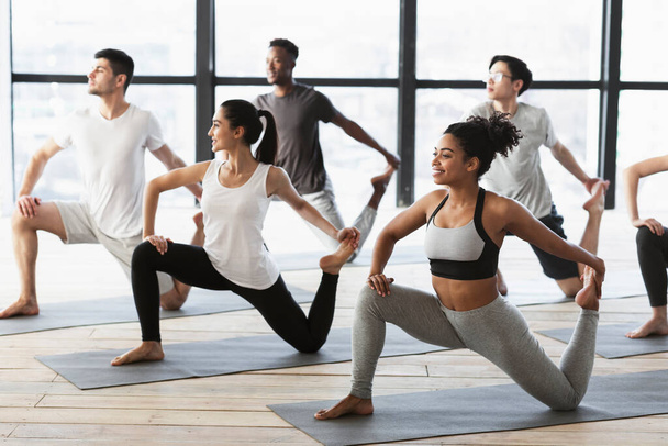 Yoga practice. Group of interracial young people doing Mermaid pose - Foto, immagini