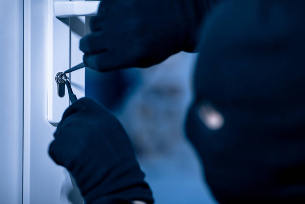 Robber in black mask cracking door with metal picklock - Φωτογραφία, εικόνα