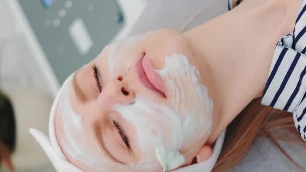 Medium shot of Beautician putting cream mask on womans face at beauty salon - Footage, Video