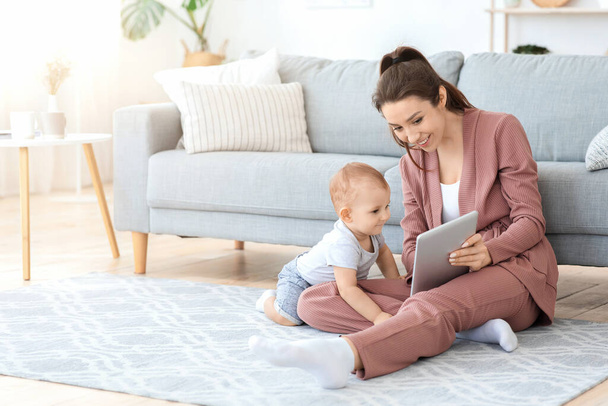 Jonge moeder en haar zoontje spelen met digitale tablet thuis - Foto, afbeelding