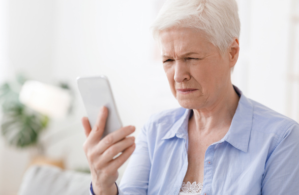 Myopia Concept. Elderly woman squinting while looking at smartphone screen - Fotografie, Obrázek