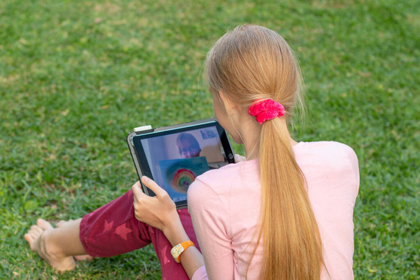 Vídeo chat concept- uma adolescente sentada em uma grama verde com um tablet
 - Foto, Imagem
