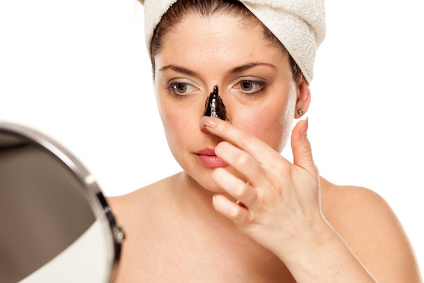 Young beautiful woman with towel on her head applying black mask on her nose - Foto, afbeelding