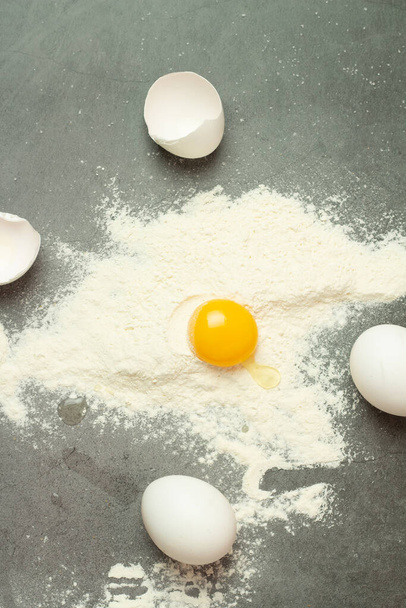 flour and broken egg, and white eggs on a black background - Фото, изображение