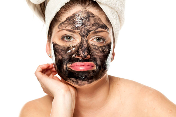jonge ongelukkige vrouw met handdoek op haar hoofd poseren met zwart masker op haar gezicht - Foto, afbeelding