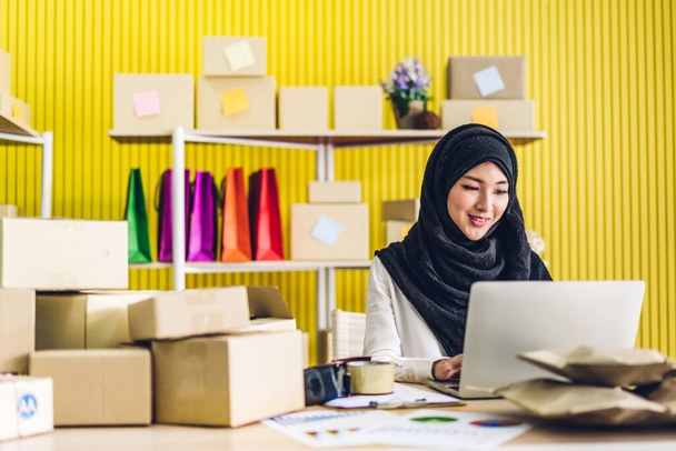 Portret uśmiechnięty piękny muzułmanin właściciel azjatycki kobieta freelancer sme biznes zakupy online praca na laptopie komputer z paczki na stole w domu - Biznes online wysyłka i dostawa - Zdjęcie, obraz