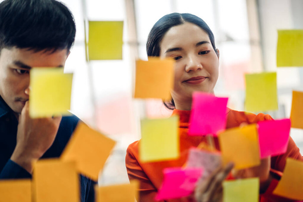 Casual creatieve gelukkig twee glimlach aziatische zakenmensen planning strategie analyse en brainstorm zetten post het stickers nota om idee te delen voor startup project op glasplaat op modern kantoor - Foto, afbeelding