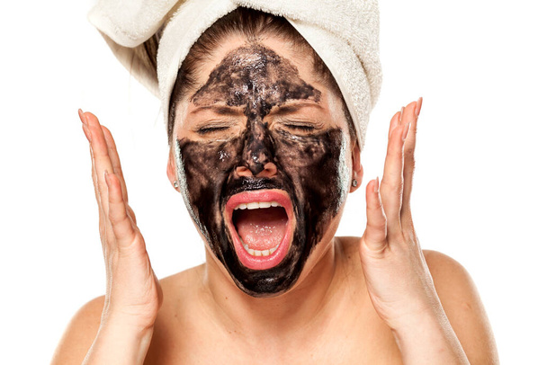 Młoda zdenerwowana kobieta z ręcznikiem na głowie pozuje z czarną maską na twarzy - Zdjęcie, obraz