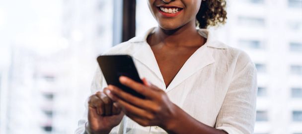 Sorridente bella donna nera africana d'affari africana professionale che lavora e utilizza smartphone in piedi in ufficio - Foto, immagini