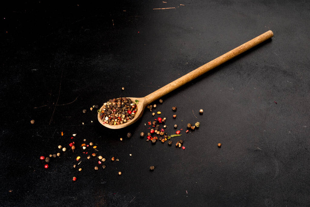 Wooden long spoon with sprinkled pepper on a black background - Foto, Imagen