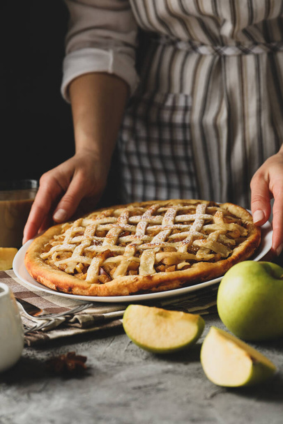 A háziasszony finom almás pitét tart a szürke asztalon. Házi készítésű étel - Fotó, kép