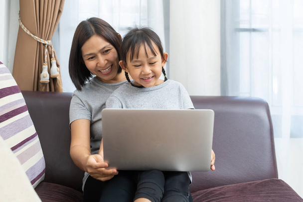 Asian mother and daughter using laptop studying homework online lesson at home, Social distance online education idea concept - Foto, Bild