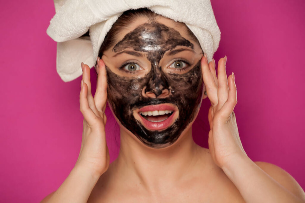 Młoda piękna kobieta z ręcznikiem na głowie pozuje z czarną maską na twarzy - Zdjęcie, obraz