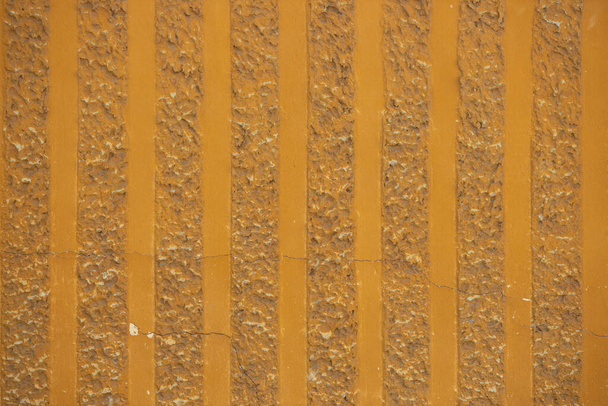 Decorativo sfondo trama parget. Frammento di parete con motivo a strisce verticali. Intonaco strutturale, superficie ruvida e irregolare di colore giallo arancio
. - Foto, immagini