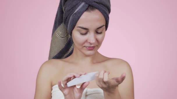 Woman in bath towel makes manicure with nail file isolated on pink background - Video