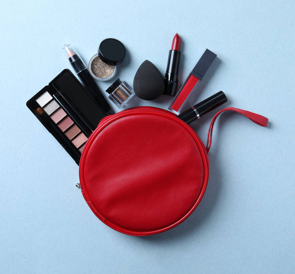 Cosmetic bag with makeup products on light blue background, flat lay - 写真・画像