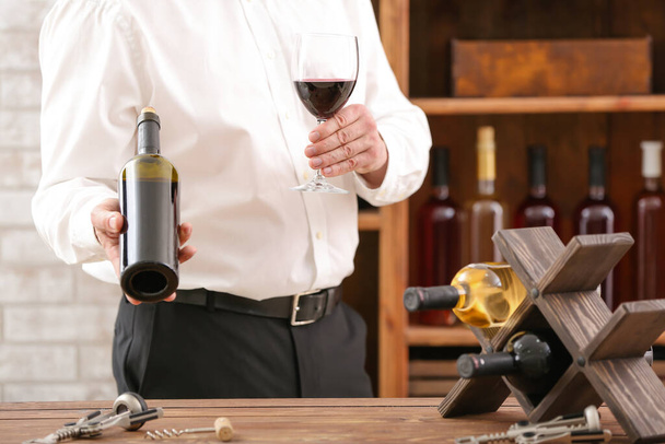 Hombre con botella y copa de sabroso vino en bodega
 - Foto, Imagen