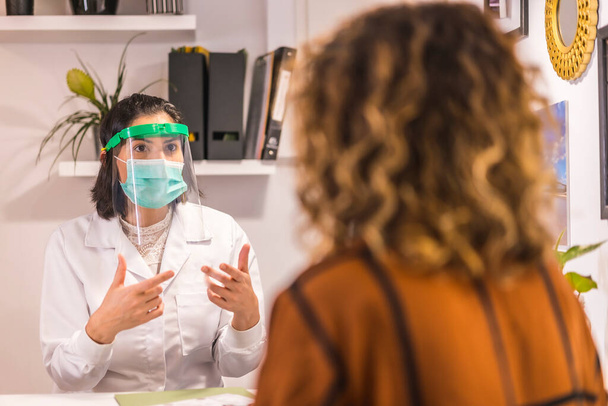 Beauty Salon, reopening after the coronavirus pandemic with security measures. Doctor with protective screen and face mask in a conversation with the client. Covid-19 - Fotoğraf, Görsel