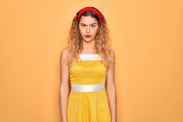 Beautiful blonde pin-up woman with blue eyes wearing diadem standing over yellow background skeptic and nervous, frowning upset because of problem. Negative person. - Photo, Image
