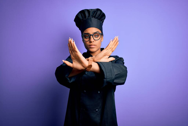 Young african american chef girl wearing cooker uniform and hat over purple background Rejection expression crossing arms doing negative sign, angry face - Fotó, kép