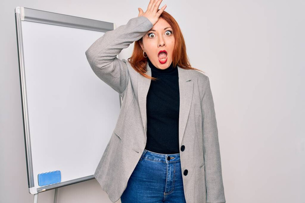 Young beautiful redhead businesswoman doing business presentation using magnetic board surprised with hand on head for mistake, remember error. Forgot, bad memory concept. - Photo, Image