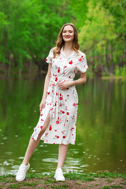 Full body portrait of a young beautiful woman in white dress posing by the lake - Photo, image