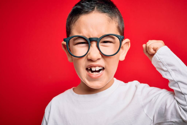 Giovane bambino intelligente ragazzo indossa occhiali nerd su sfondo rosso isolato infastidito e frustrato urlando con rabbia, pazzo e urlando con mano alzata, concetto di rabbia
 - Foto, immagini