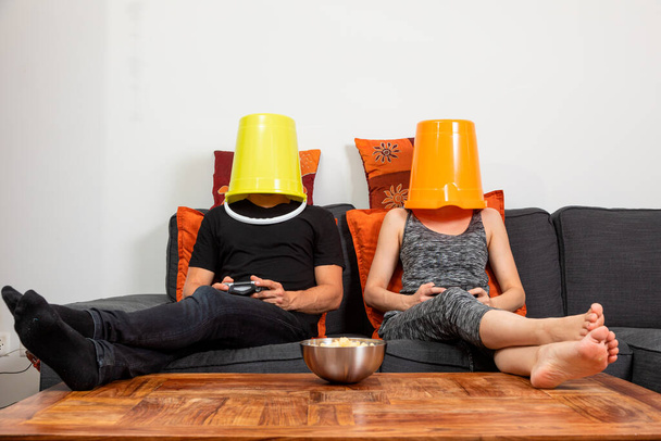 Young couple play video games sitting comfortably on the sofa at home. They drink beer and eat chips - 写真・画像