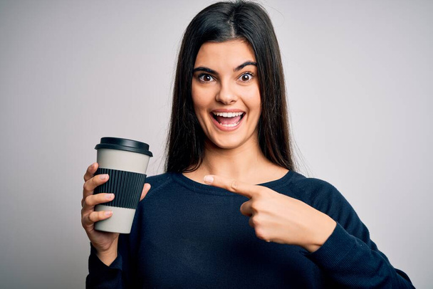 Junge schöne brünette Frau trinkt Tasse Kaffee über isolierten weißen Hintergrund sehr glücklich zeigt mit der Hand und dem Finger - Foto, Bild